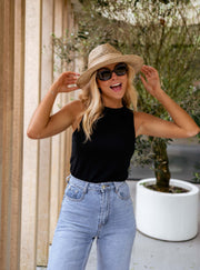 Top moulant col rond noir porté par une femme, silhouette entière, chapeau de paille, lunettes