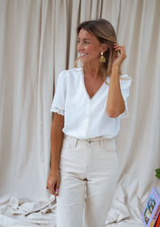 Blouse col V manches brodées portée par une femme, vue de trois-quarts, main dans les cheveux