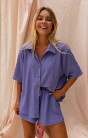 Chemise fluide à manches courtes portée par une femme, silhouette entière, rideaux roses, short assorti