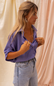 Chemise fluide à manches courtes portée par une femme, vue de trois-quarts, jean clair, main au col