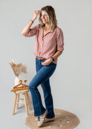 Blouse vichy à petits cœurs portée par une femme, vue de trois-quarts, main sur la tête, jean flare