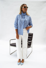 Chemise opaque à col victorien bleue portée par une femme, vue de face, chaise métallique, lunettes de soleil