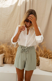 Chemise à col et boutons portée par une femme, vue de trois-quarts, main sur la tête