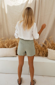 Chemise à col et boutons portée par une femme, vue de dos, coussins, short vert sauge