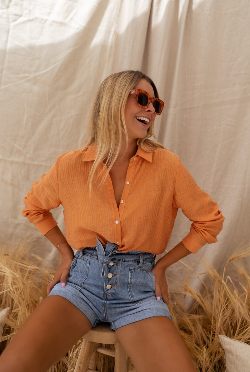 Chemise fluide à col classique portée par une femme, silhouette entière, botte de paille, short en jean