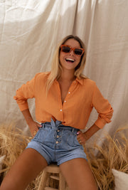 Chemise fluide à col classique portée par une femme, assise, tabouret, mains sur les hanches