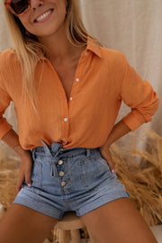 Chemise fluide à col classique portée par une femme, vue de trois-quarts, mains sur les hanches, short en jean