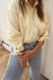 Chemise à poche fleurie portée par une femme, vue rapprochée, poignets noués, jean