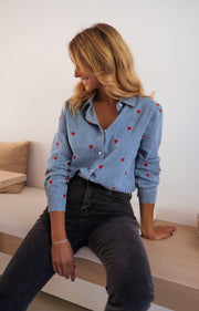 Chemise en jean à cœurs portée par une femme, vue de trois-quarts, sur un banc, jean noir