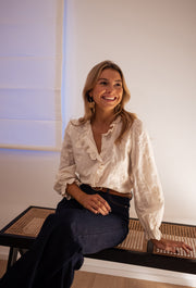 Chemise brodée à volants portée par une femme, assise, sur un banc en cannage, sourire