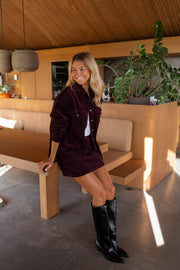 Chemise en velours ample bordeaux portée par une femme, vue de face, banc, bottes noires