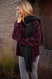 Chemise en velours ample bordeaux portée par une femme, vue de trois-quarts, écharpe noire, extérieur