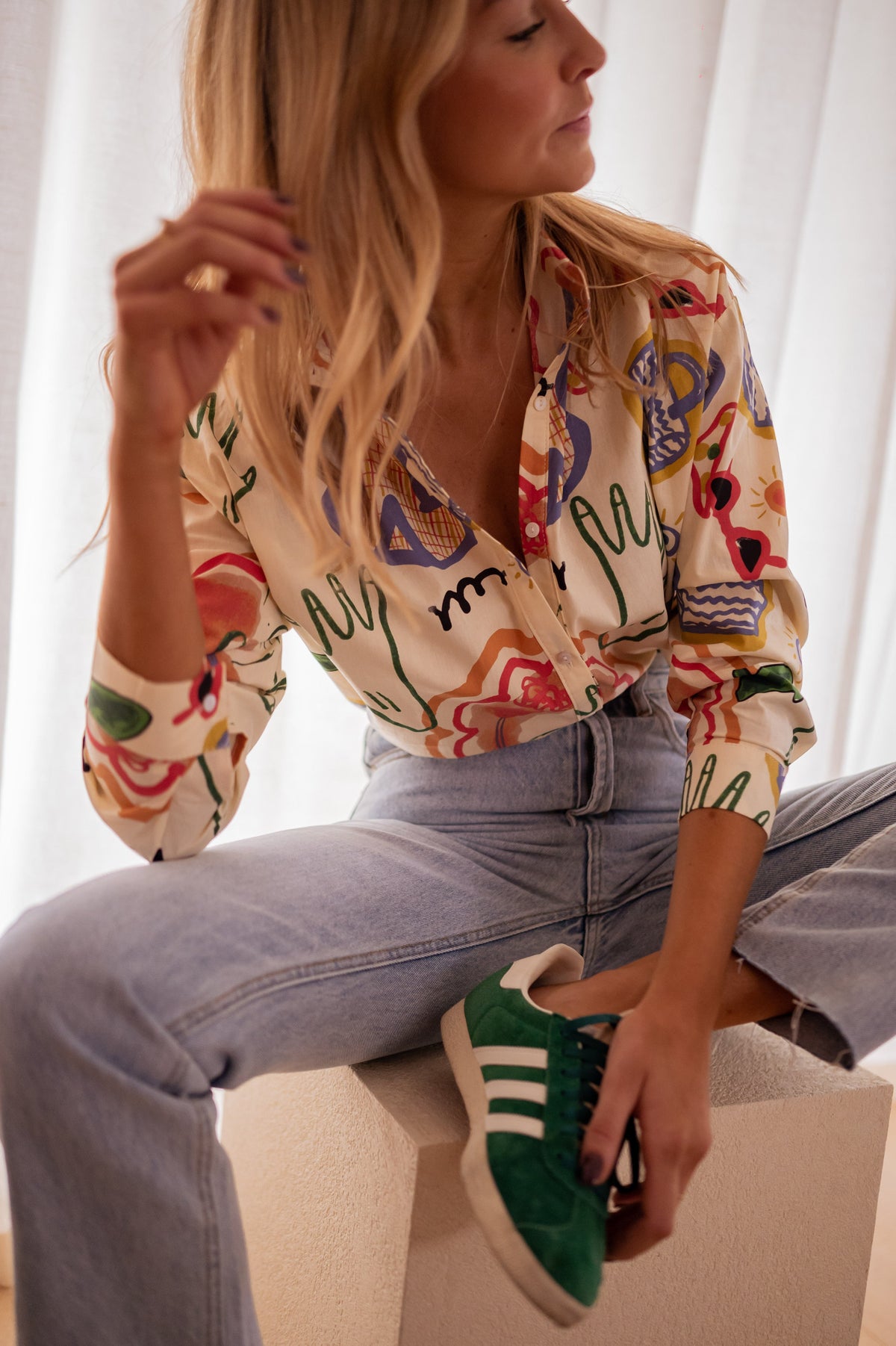 Chemise en coton à motifs portée par une femme, assise, sur un cube blanc, baskets vertes, jean clair