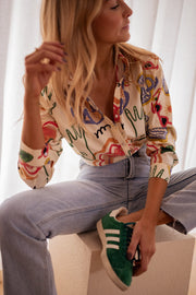 Chemise en coton à motifs portée par une femme, assise, sur un cube blanc, baskets vertes, jean clair
