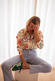 Chemise en coton à motifs portée par une femme, assise, main sur le visage, jean clair
