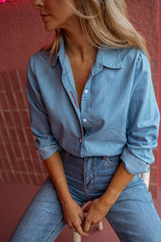 Chemise en denim fluide portée par une femme, vue rapprochée, mains sur les genoux, jean