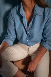 Chemise en denim fluide portée par une femme, vue rapprochée, pantalon beige, assise