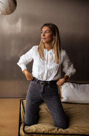 Blouse brodée en dentelle portée par une femme, à genoux sur un canapé, jean noir