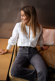 Blouse brodée en dentelle portée par une femme, assise, sourire, jean noir