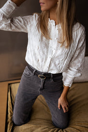 Blouse brodée en dentelle portée par une femme, vue rapprochée, bras levé, jean noir
