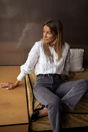 Blouse brodée en dentelle portée par une femme, assise, jean noir, coussins