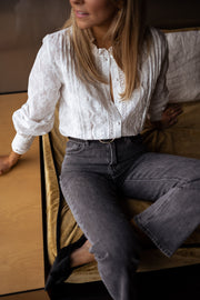 Blouse brodée en dentelle portée par une femme, assise, sur un canapé, bras relevé