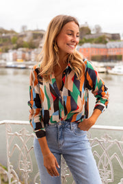 Chemise fluide à motifs multicolore portée par une femme, vue de face, balustrade, jean