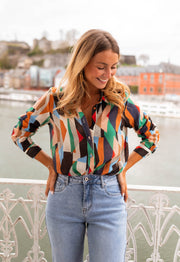 Chemise fluide à motifs multicolore portée par une femme, vue de face, balustrade blanche, jean