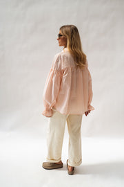 Chemise fluide à poignets élastiques portée par une femme, vue de dos, fond blanc, pantalon écru