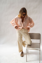 Chemise fluide à poignets élastiques portée par une femme, vue de trois-quarts, chaise grise, jambe levée
