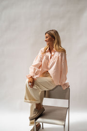 Chemise fluide à poignets élastiques portée par une femme, assise, chaise grise, pantalon écru