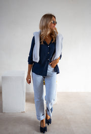 Chemise fluide en coton portée par une femme, silhouette entière, pull gris sur les épaules, jean
