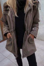Manteau imperméable à capuche fourrée porté par une femme, vue rapprochée, cordon de serrage à la taille
