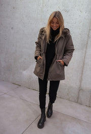 Manteau imperméable à capuche fourrée porté par une femme, silhouette entière, capuche relevée, bottines noires