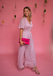 Robe longue à lurex brillant portée par une femme, vue de face, fond rose, pochette fuchsia
