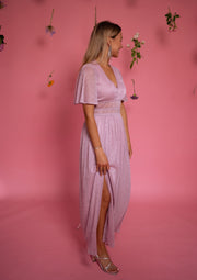 Robe longue à lurex brillant portée par une femme, vue de trois-quarts, fond rose, fente