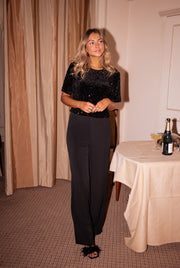 Combinaison fluide à buste pailleté portée par une femme, silhouette entière, pantalon noir, nappe