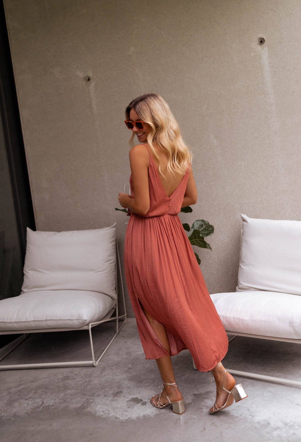Robe fluide effet soie fendue portée par une femme, en marchant, terrasse, fauteuils blancs