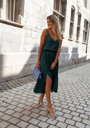 Robe fluide effet soie portée par une femme, vue de face, façade en pierre, pochette bleue