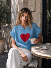 Pull bleu clair cœur rouge — vue portée assise à une table en terrasse, tasse blanche