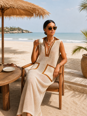 Robe maxi beige à blocs — vue portée assise à une table en bois sur la plage, lunettes de soleil