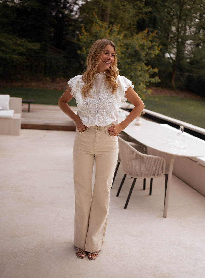 Jean évasé taille haute beige porté par une femme, silhouette entière, terrasse, chaises