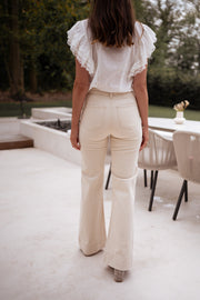 Jean évasé taille haute beige porté par une femme, vue de dos, terrasse, haut blanc