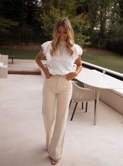 Jean évasé taille haute beige porté par une femme, vue de face, mains sur les hanches, jardin
