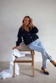 Gilet à boutons porté par une femme, assise, sur une chaise, drap blanc