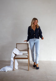Gilet à boutons porté par une femme, silhouette entière, chaise en bois, jean clair