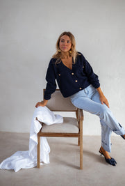 Gilet à boutons porté par une femme, assise, sur une chaise en bois, jambes croisées