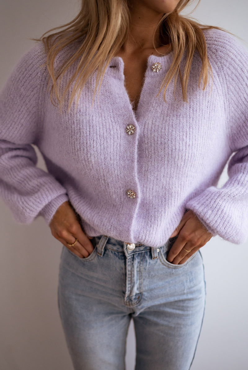 Gilet à boutons fleuris brillants porté par une femme, vue rapprochée, mains dans les poches, jean clair