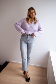 Gilet à boutons fleuris brillants porté par une femme, silhouette entière, jean clair, escarpins noirs, mur blanc