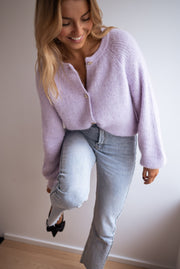 Gilet à boutons fleuris brillants porté par une femme, vue de trois-quarts, jambe levée, jean clair